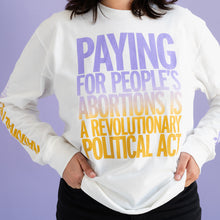 Load image into Gallery viewer, A person with wavy brown hair sports a long sleeved white tee that reads PAYING FOR PEOPLE&#39;S ABORTIONS IS A REVOLUTIONARY POLITICAL ACT, with their hands on their hips. The model&#39;s face is cropped out of frame.

