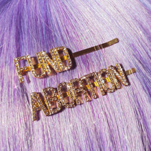 Load image into Gallery viewer, Two gold hairpins with sparkly rhinestone letters that, together, read FUND ABORTION. The pins are displayed in straight hair that is lavender in color.
